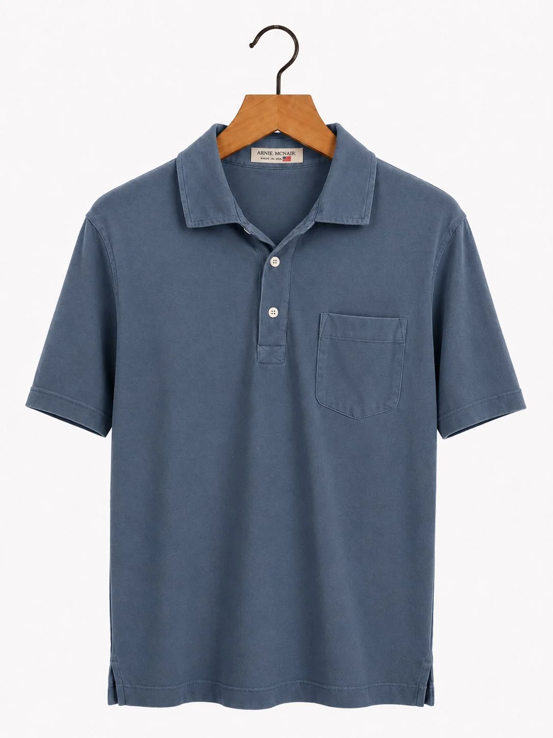 An Arnie McNair pocket polo in slate blue on a wooden hanger, showing the two-button placket and woven neck label.