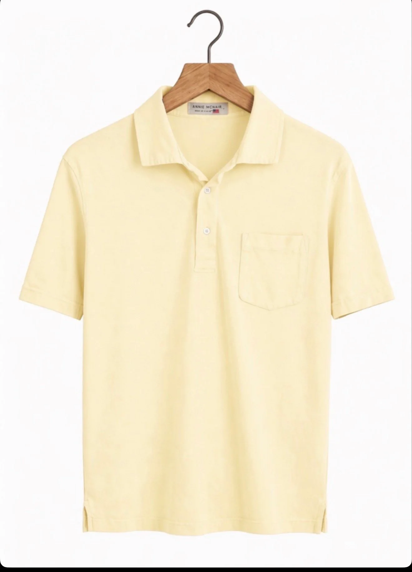 An Arnie McNair pocket polo in butter yellow on a wooden hanger, showing the spread collar and chest pocket.