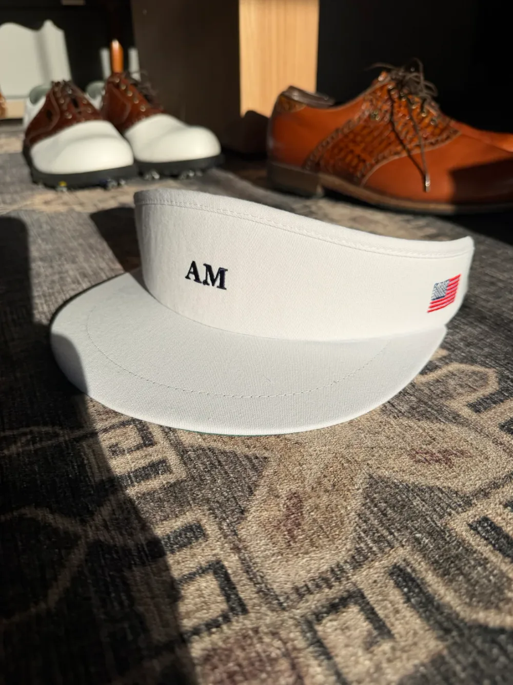 White Arnie McNair AM visor with an American flag, beside classic leather golf shoes
