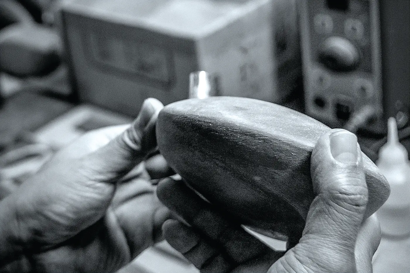 Black and white close-up of a craftsman's hands shaping a wooden driver head.