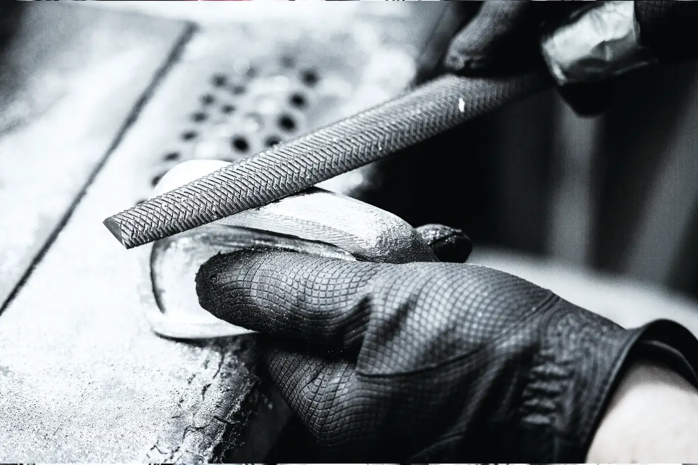 Black and white close-up of a gloved hand filing an iron head.