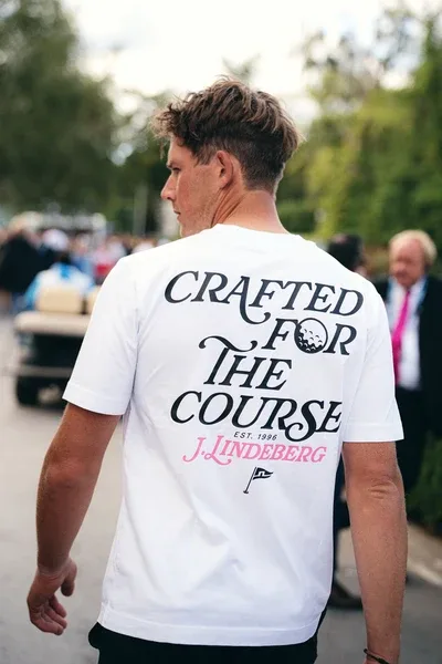 A man seen from behind wearing a white J.Lindeberg T-shirt printed Crafted for the Course.