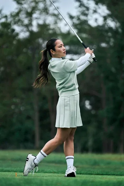 A golfer in a pale green J.Lindeberg top and pleated skirt holding her finish.