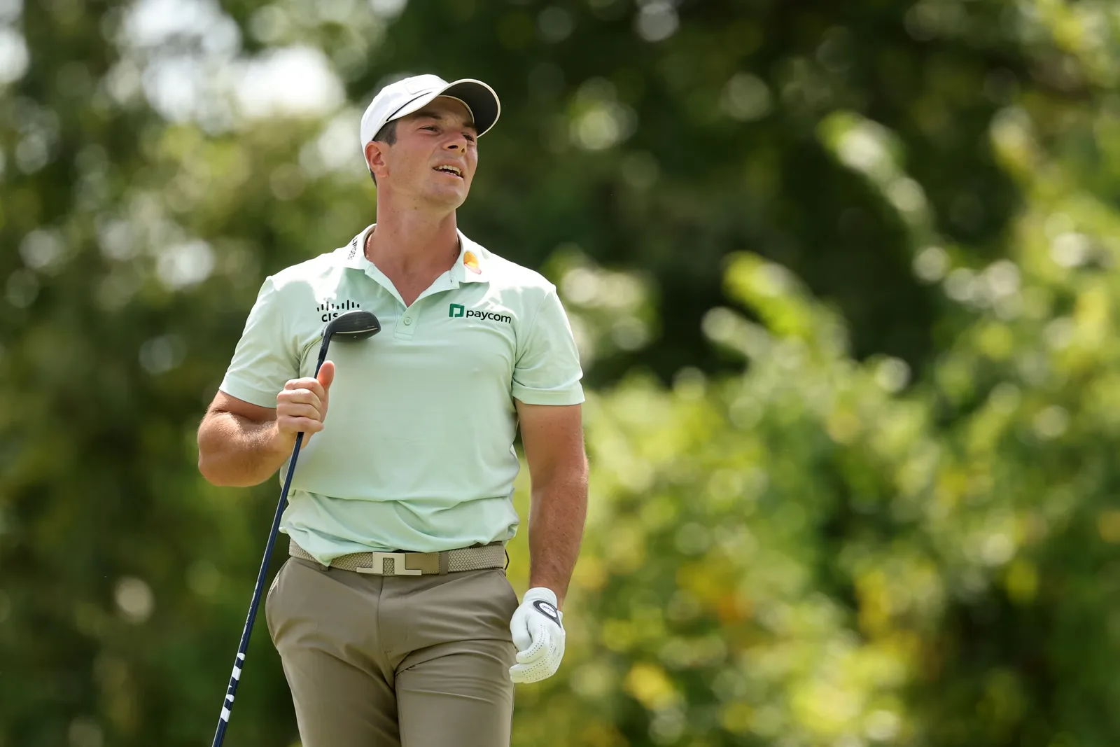 Viktor Hovland in a mint green polo holding a club on a golf course.