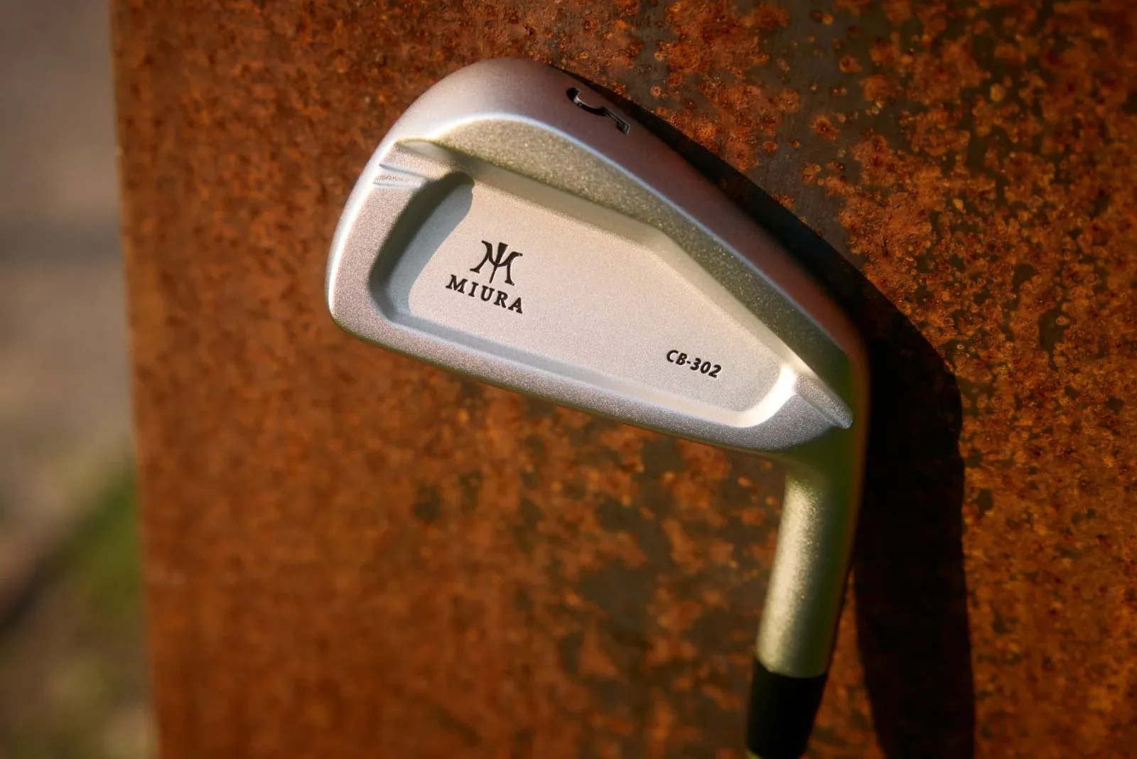 A Miura CB-302 iron in white chrome leaning against a rusted steel wall.