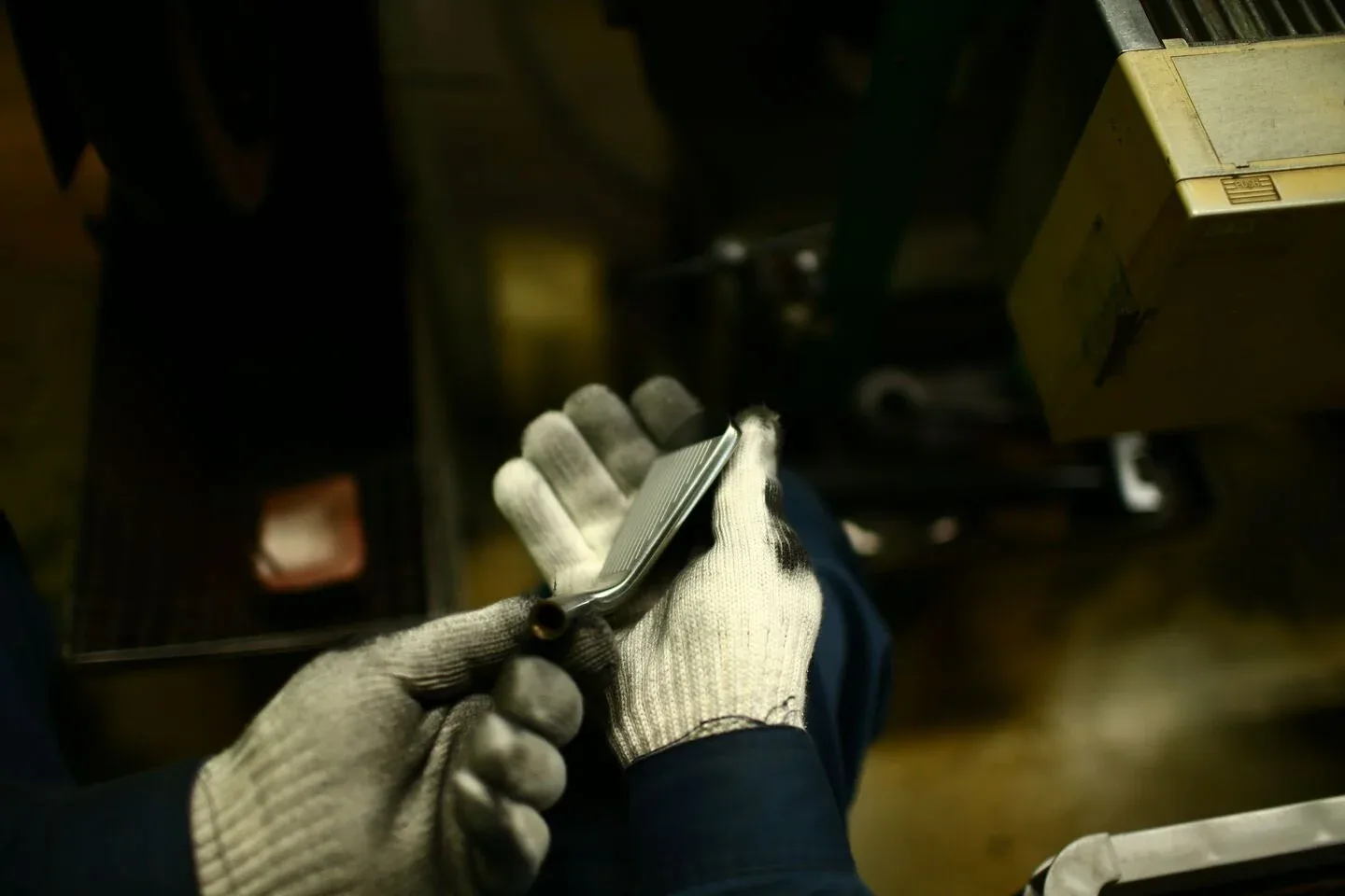 Gloved hands inspecting a forged iron head in a dark workshop.