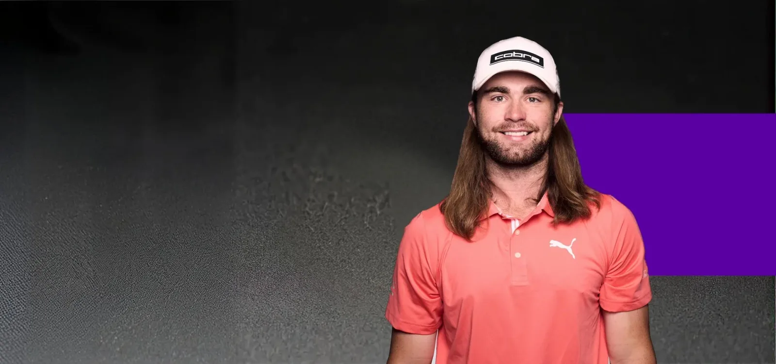 Kyle Berkshire smiling in a white Cobra cap and a coral Puma polo against a dark backdrop with a purple panel.