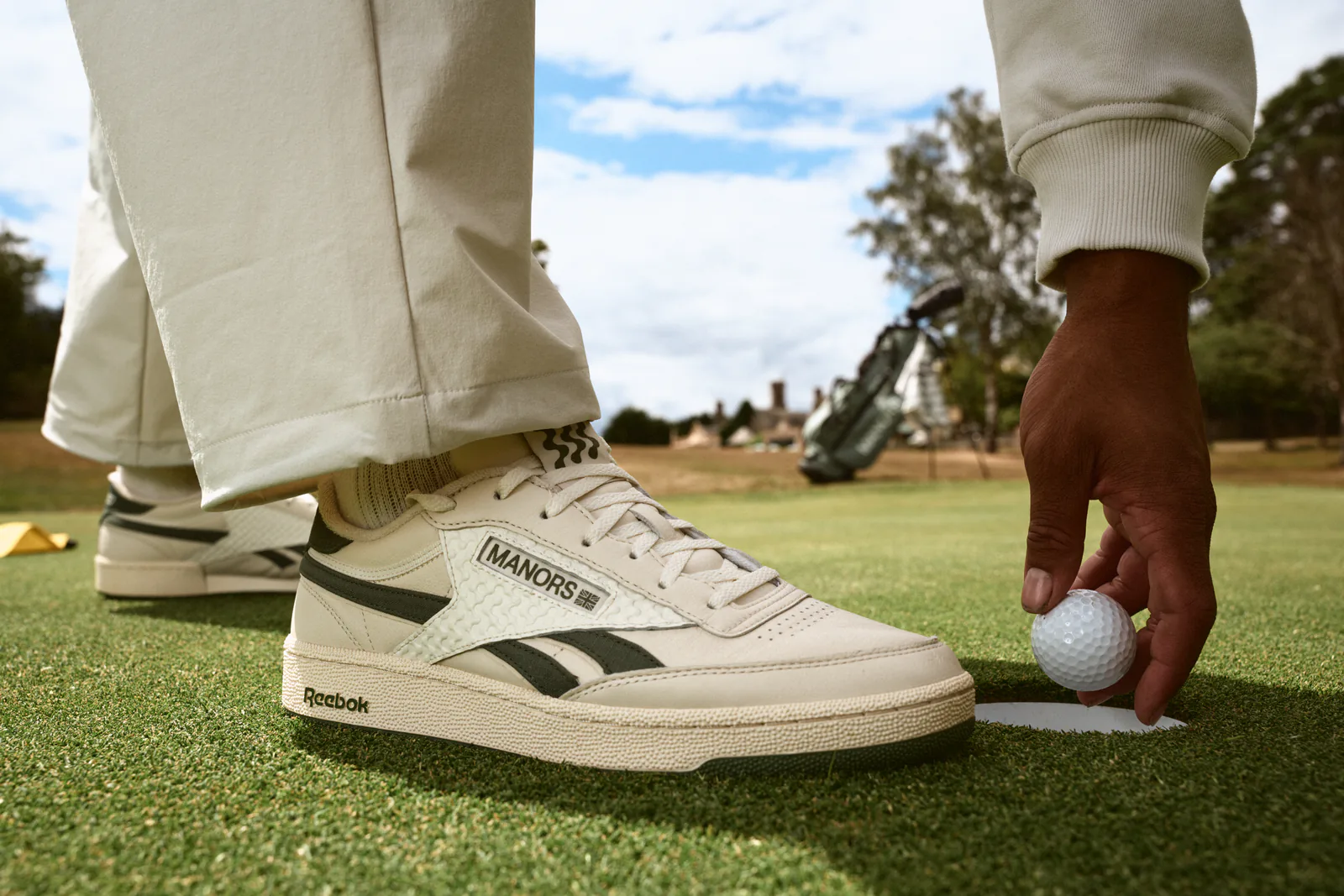 Reebok x MANORS Club C Revenge Golf shoe worn on grass, cream leather upper with Reebok side stripe.