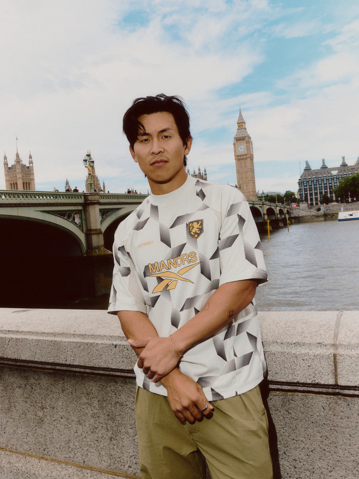 Model wearing the Reebok x MANORS mock neck polo on the bank of the Thames with the Palace of Westminster behind.