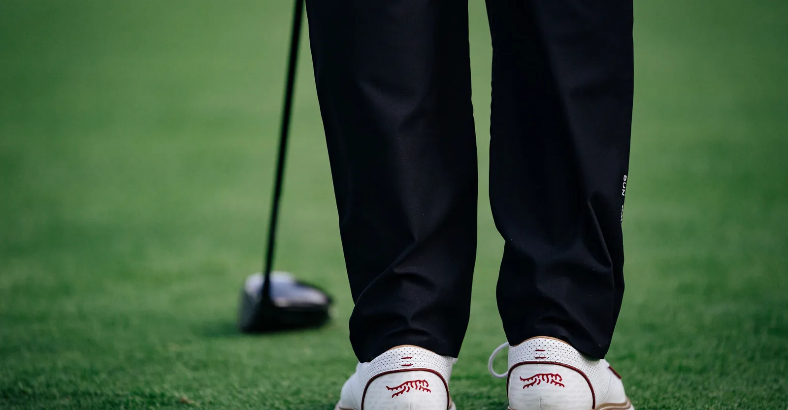 Close view of a golfer in Sun Day Red golf shoes standing over a driver.