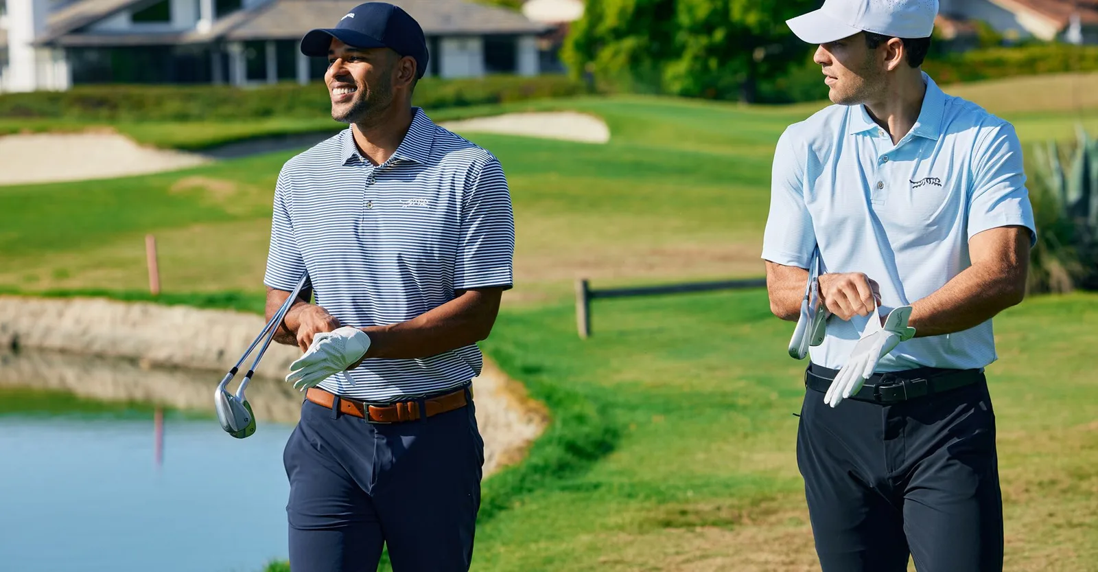 Two golfers in Sun Day Red polos walking beside a pond on a golf course.