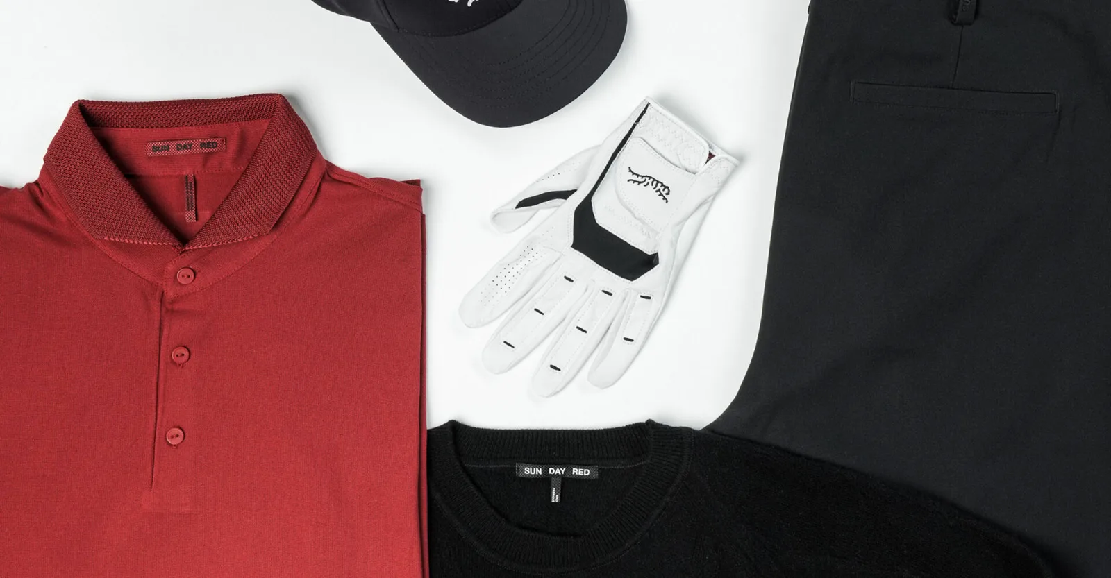A red Sun Day Red polo laid flat beside a black cap, a white glove and a black T-shirt.