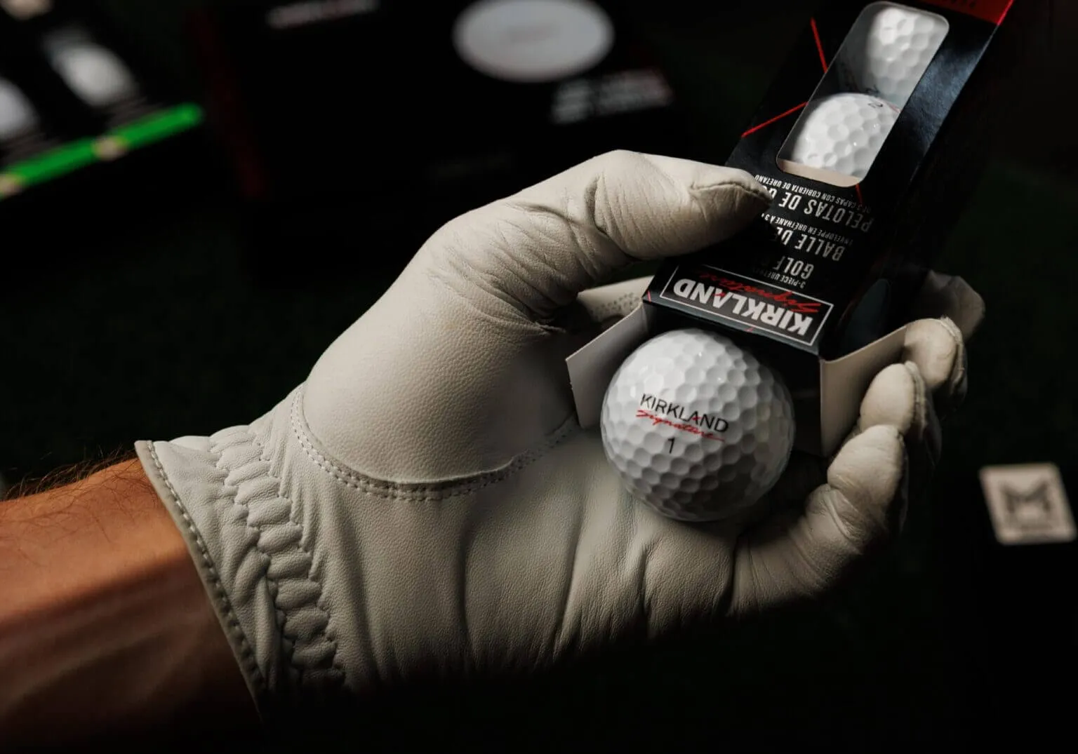 A gloved hand taking a white Kirkland Signature ball out of its sleeve.
