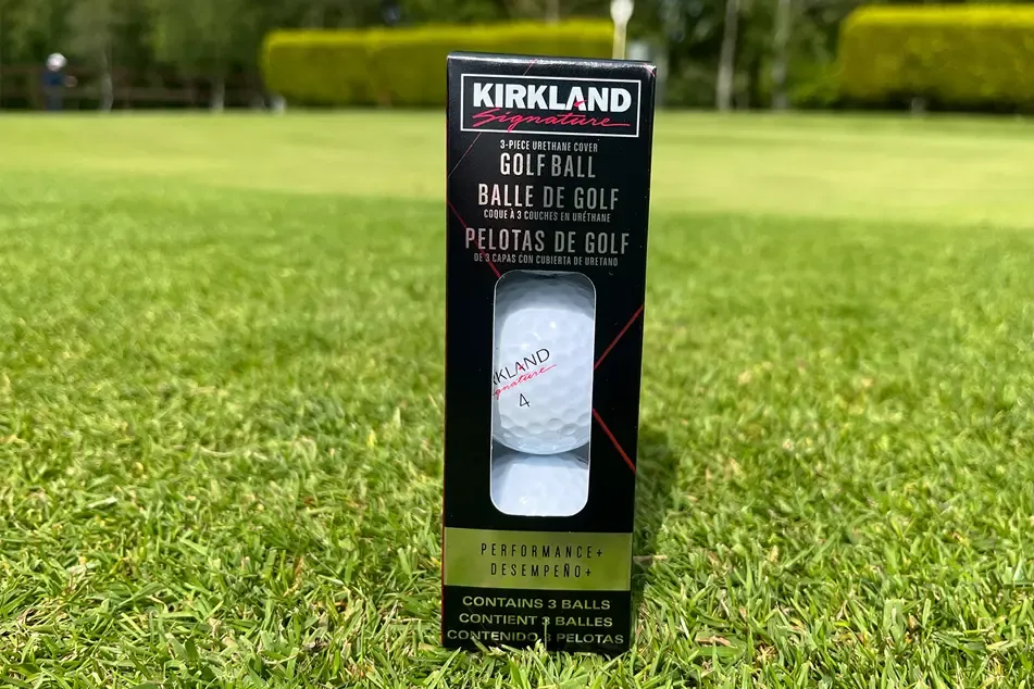 A three-ball sleeve of Kirkland Signature golf balls standing on a fairway.