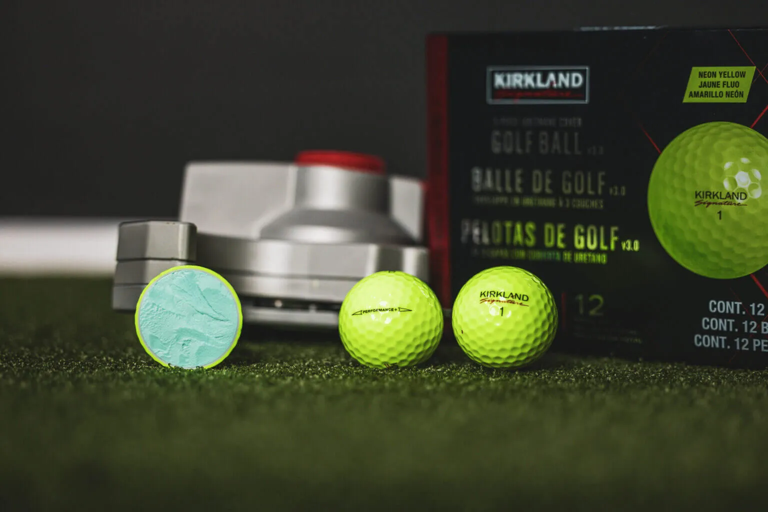 A yellow Kirkland golf ball cut in half beside two whole yellow balls and a Kirkland box.