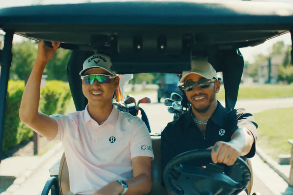 Lewis Hamilton driving a golf cart in Lululemon golf apparel alongside a playing partner
