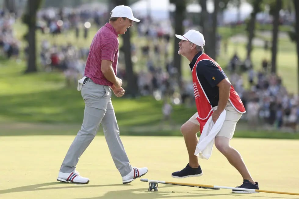 A U.S. player in a striped red polo and his caddie in a red Presidents Cup bib celebrating face to face on a green at Medinah